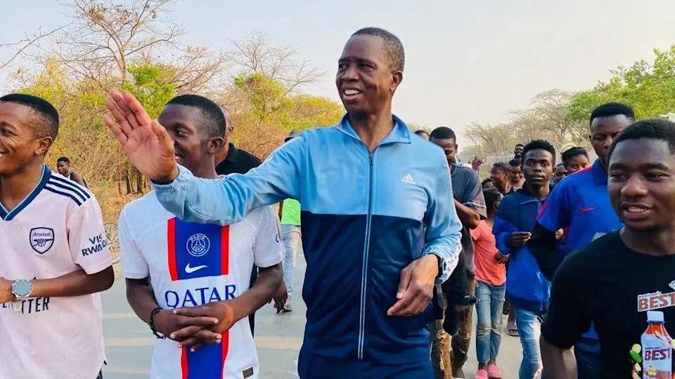 Edgar Lungu in a tracksuit waving. He is surrounded by a group as he runs outside.