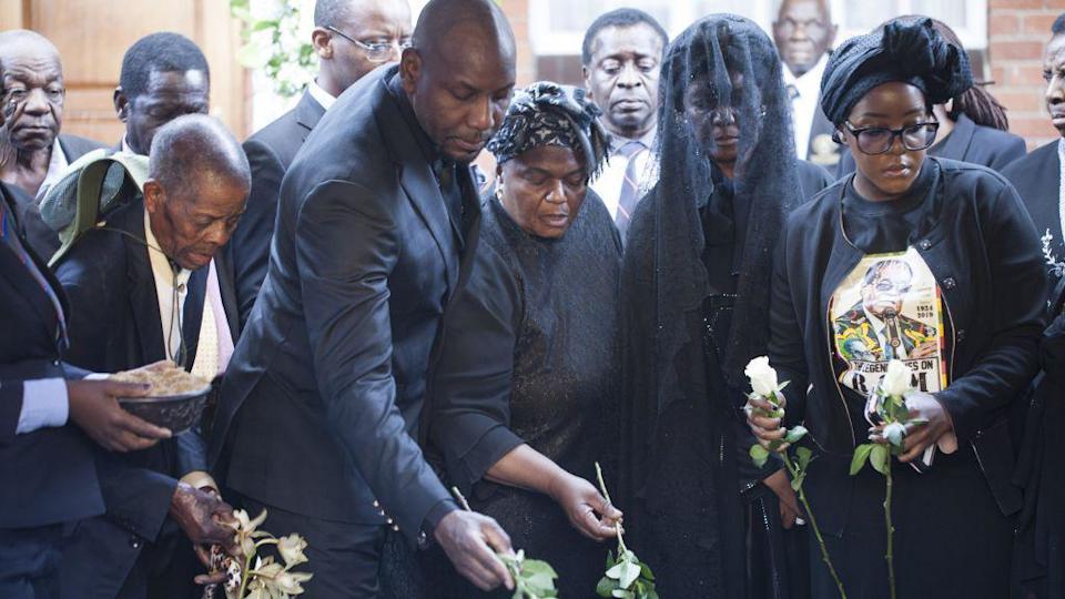 Robert Mugabe's family, dressed in black, lay flowers on his coffin at his burial.